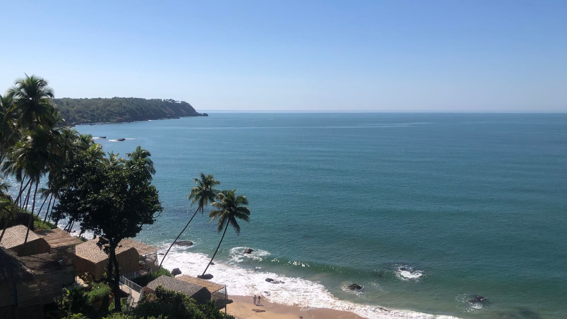 Palm-fringed cliffside view over the Arabian Sea with a beach shack and rocky headland, Goa