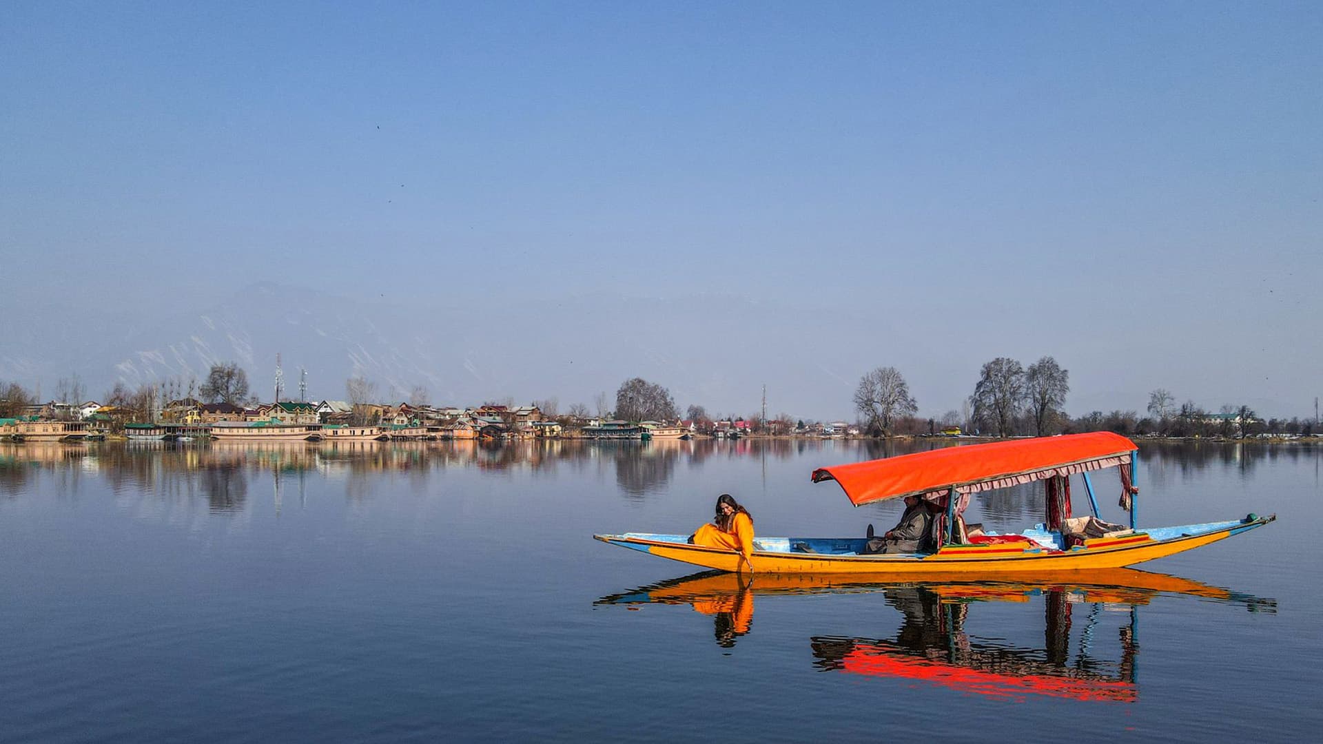 Shikara boat with an orange canopy on Dal Lake, houseboats and the Himalayan foothills behind, Srinagar
