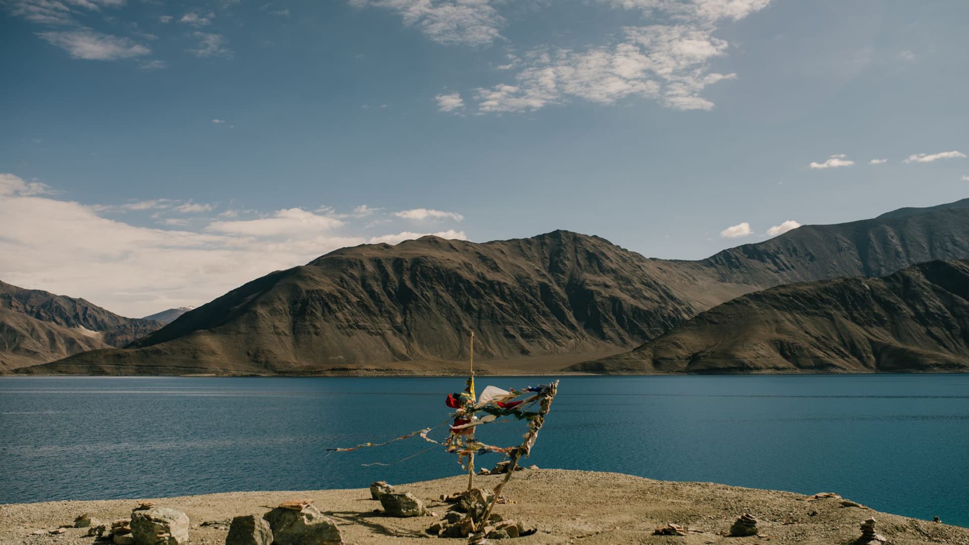 Prayer flags on the rocky shore of Pangong Lake with mountains reflected in the blue water