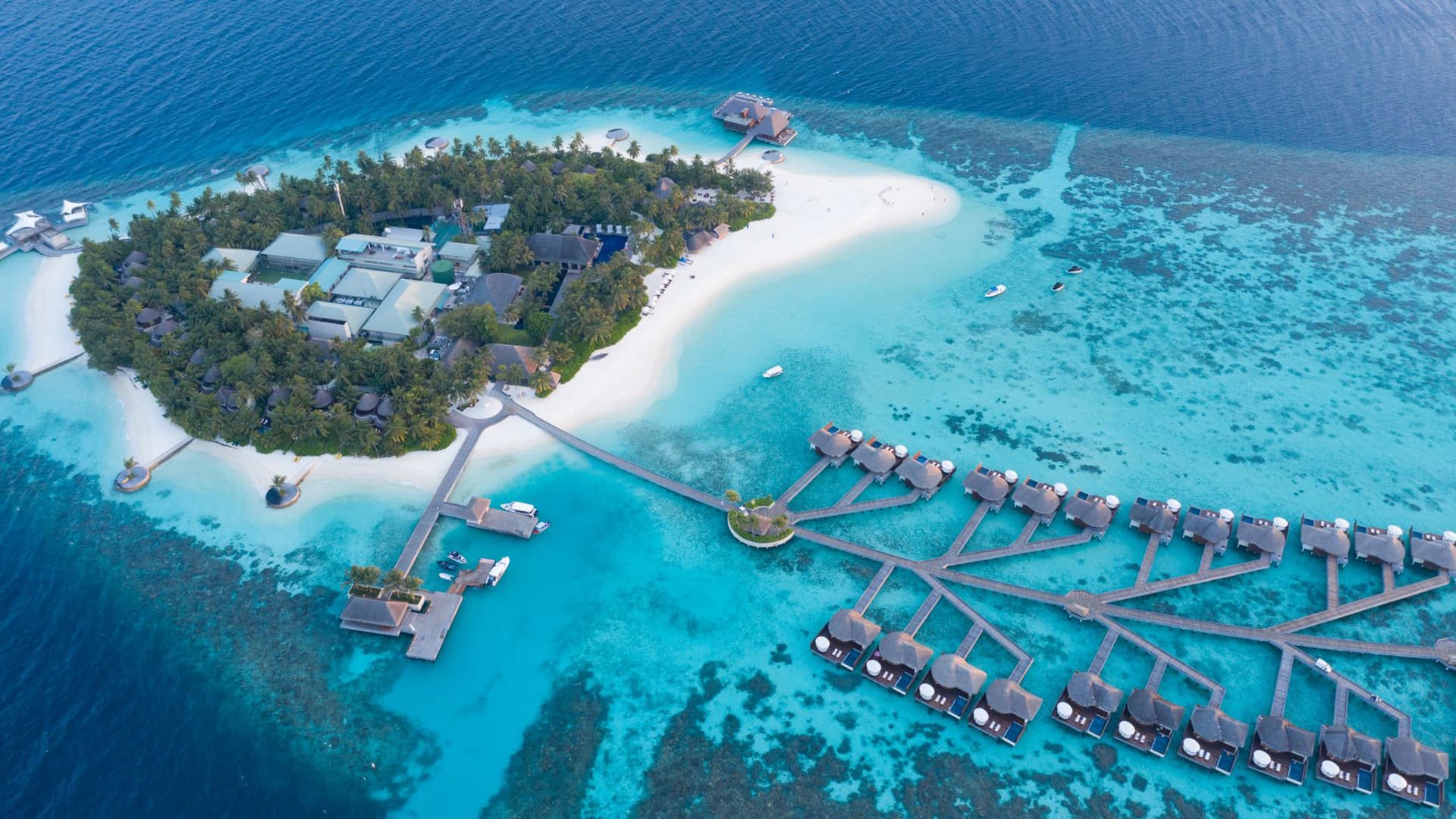 Aerial view of an overwater villa resort with a turquoise lagoon and coral reef, Maldives
