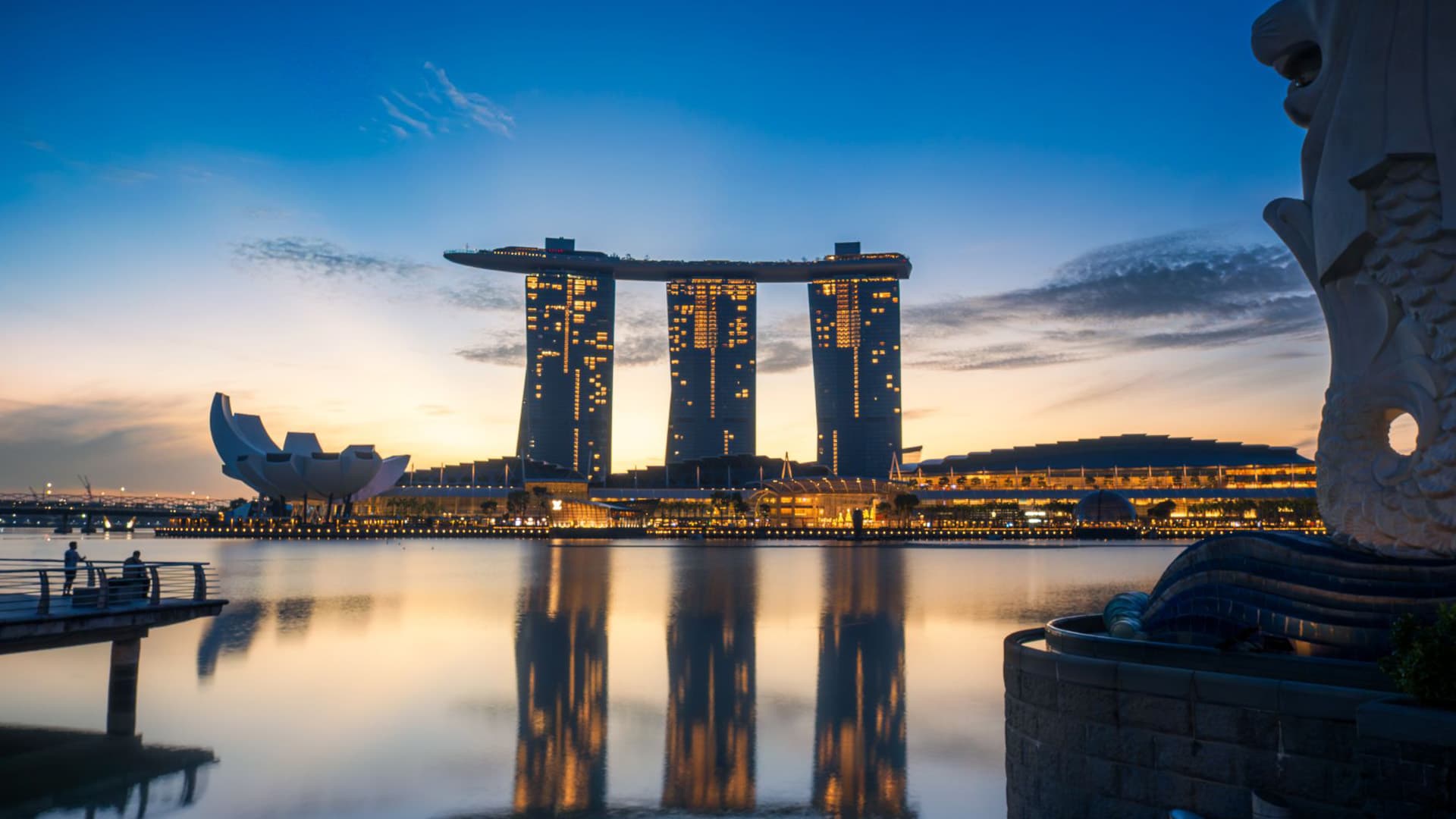 Marina Bay Sands towers lit up at dusk and reflected in the water, with the Merlion statue in the foreground, Singapore