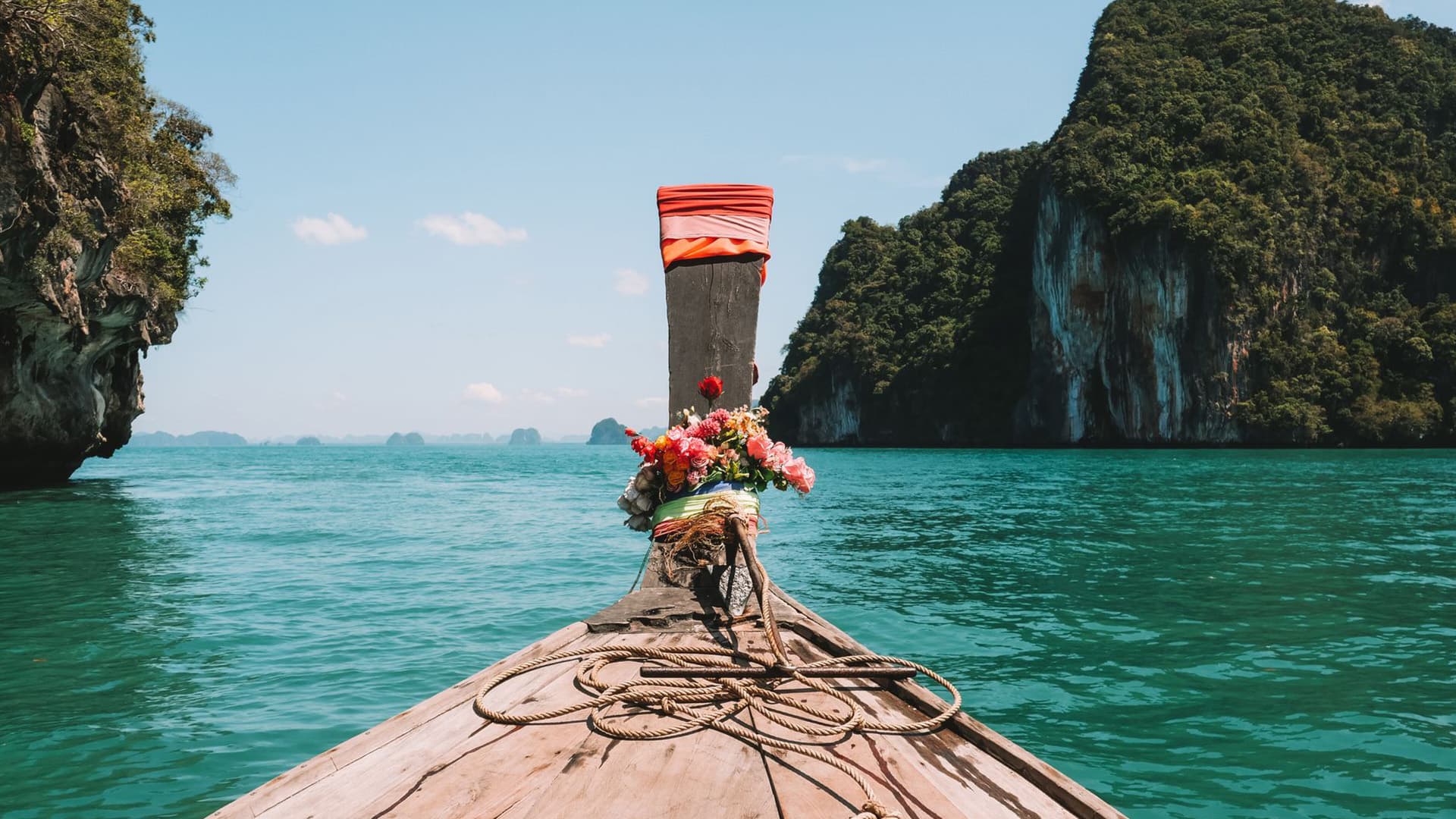 View from the bow of a flower-adorned longtail boat approaching limestone islands in Phang Nga Bay