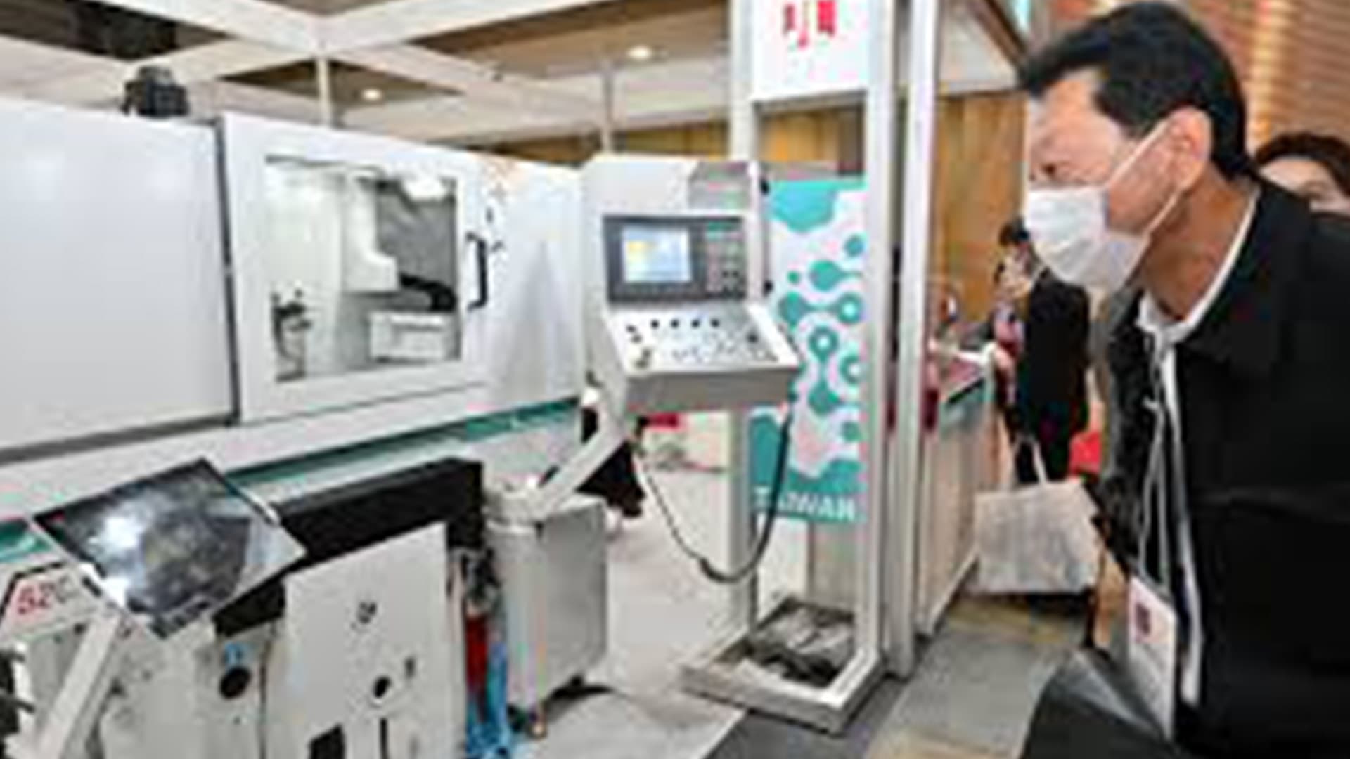 Visitors examining a CNC machine tool exhibit on the show floor at a Tokyo machine tool fair