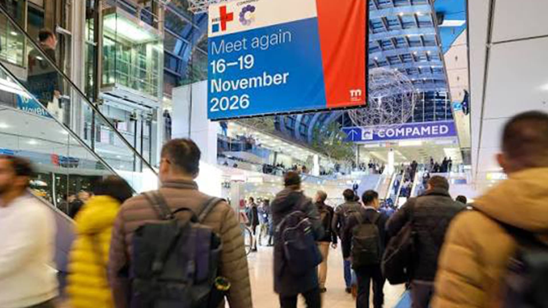 Attendees in Messe Düsseldorf's atrium beneath a MEDICA 2026 dates banner, next to COMPAMED signage